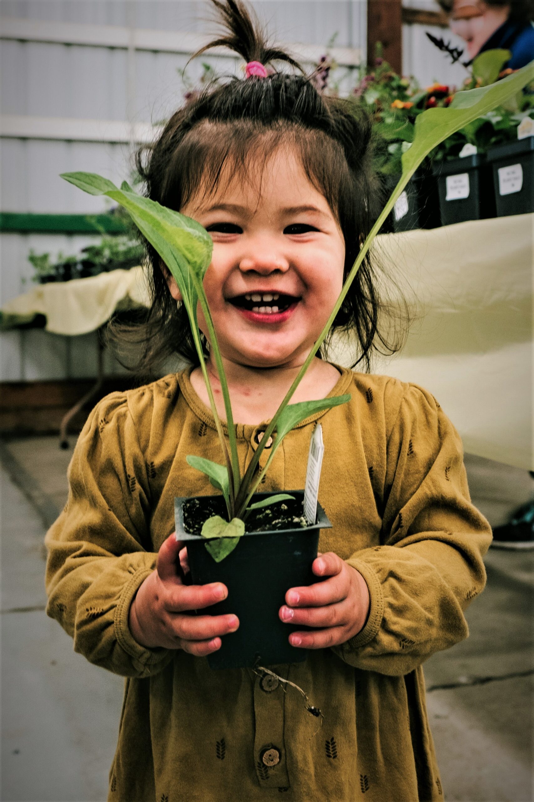 A young child smiling and holding a plant.