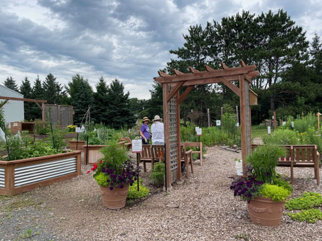 Garden entrance with raised beds, benches, potted plants and gravel paths